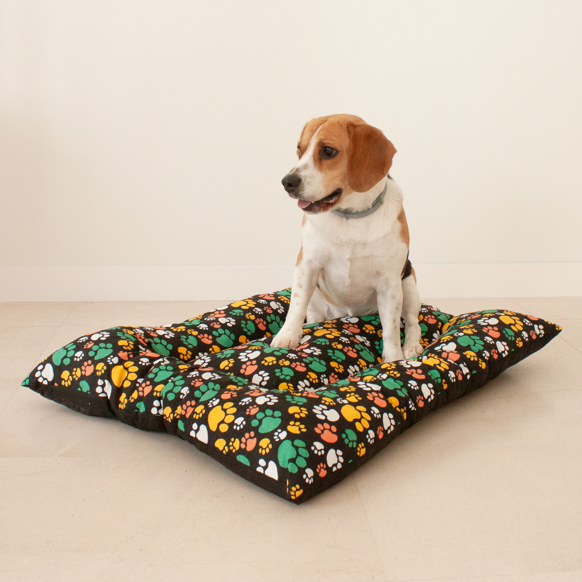 Almofada grande acolchoada para animais de estimação. Preta com estampas de patas multicoloridas. 85x70x10 cm