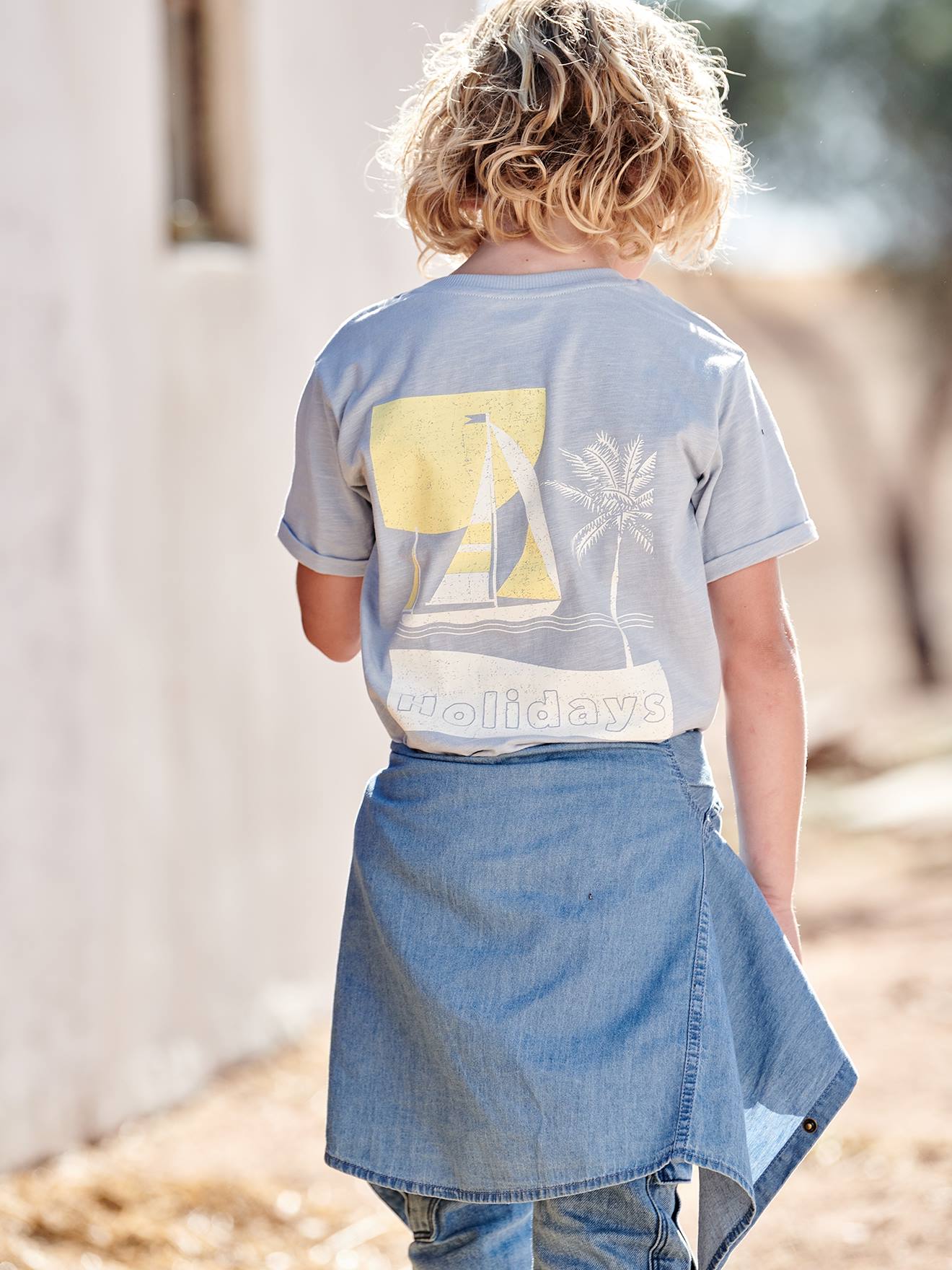Camiseta azul-clara infantil com estampa grande de barco nas costas.