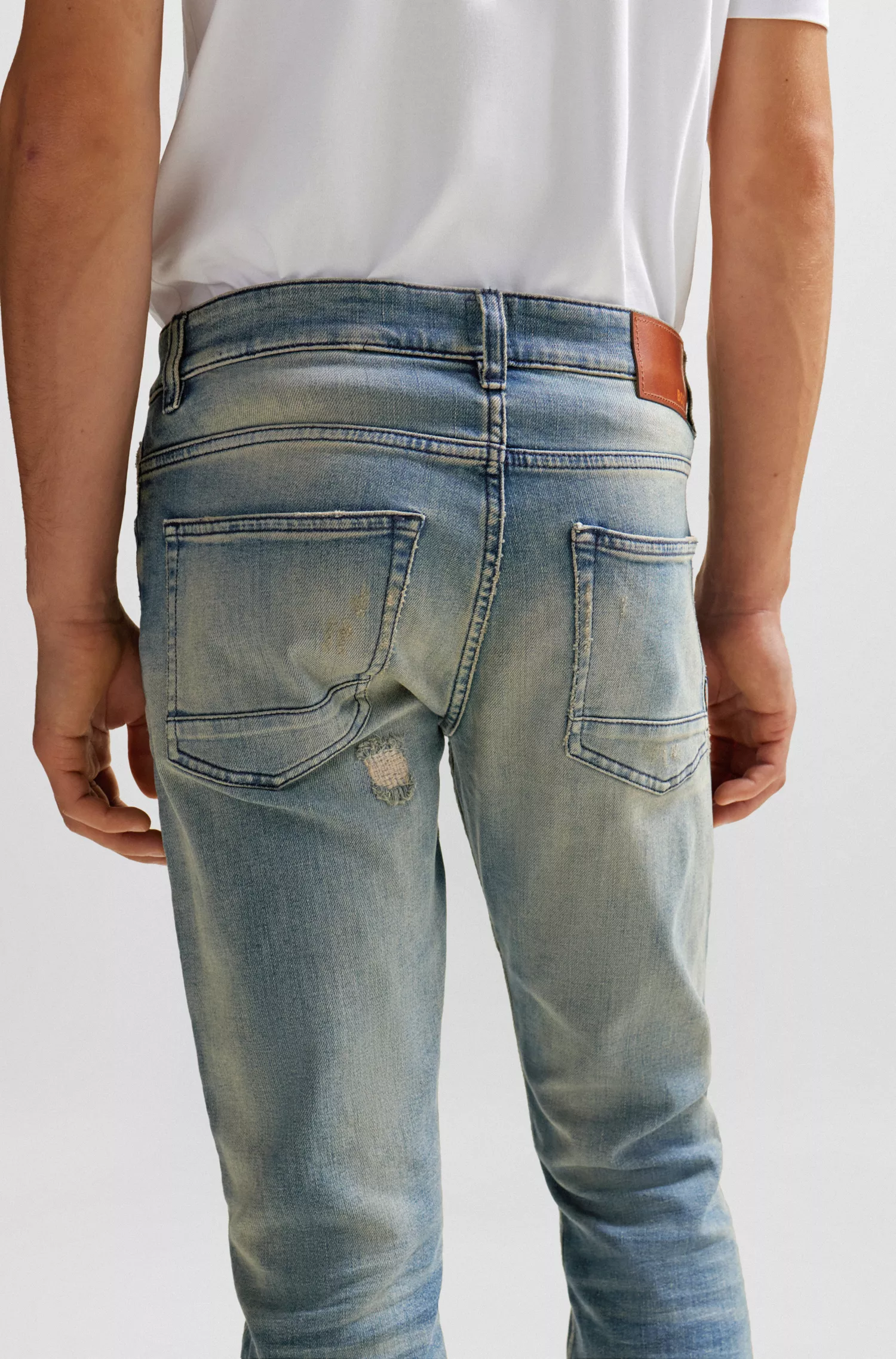 Calça jeans BOSS laranja, corte slim, em denim azul com tonalidade bege.