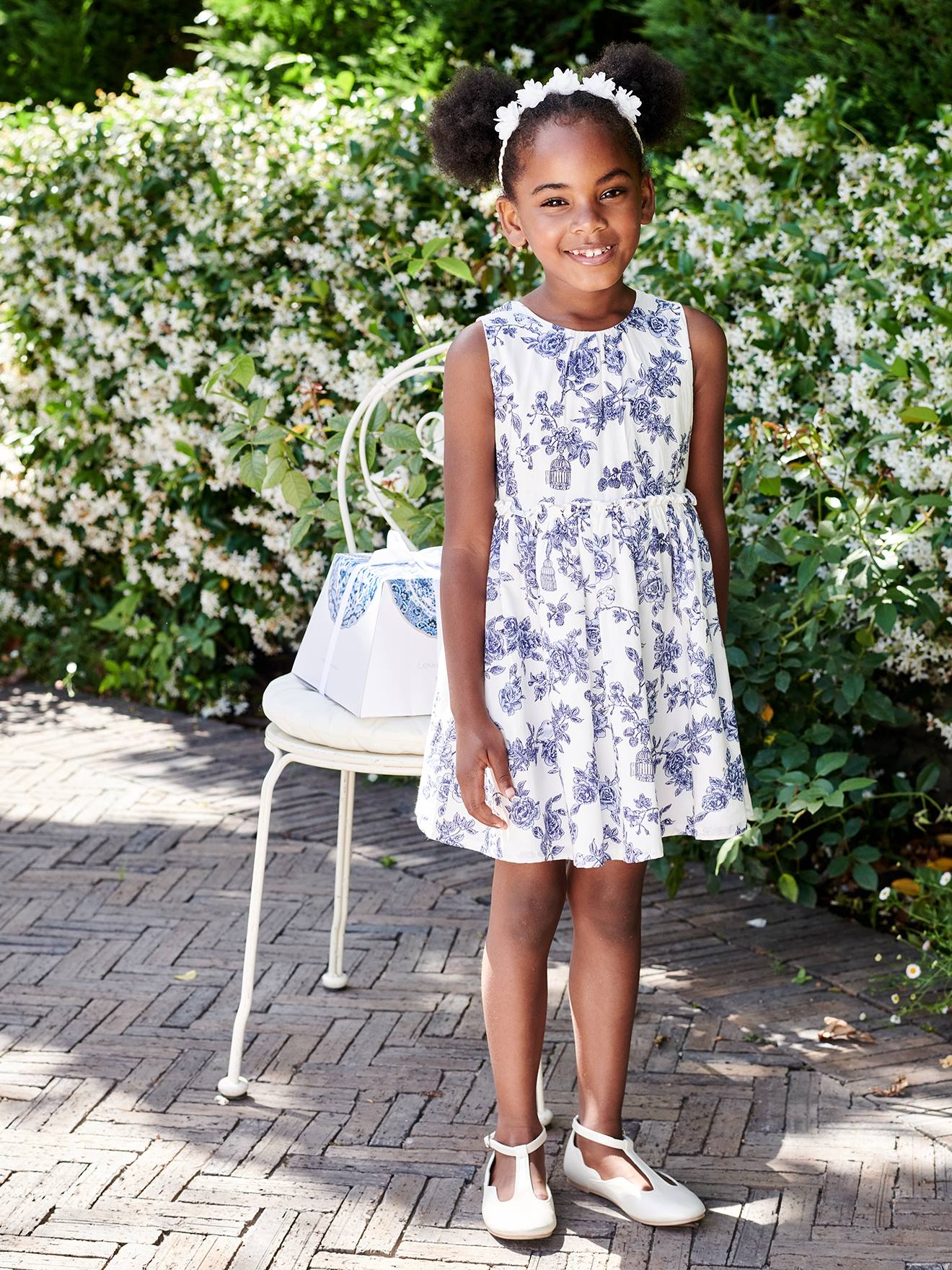 Vestido de festa infantil com flores e laço nas costas, na cor branco-creme.