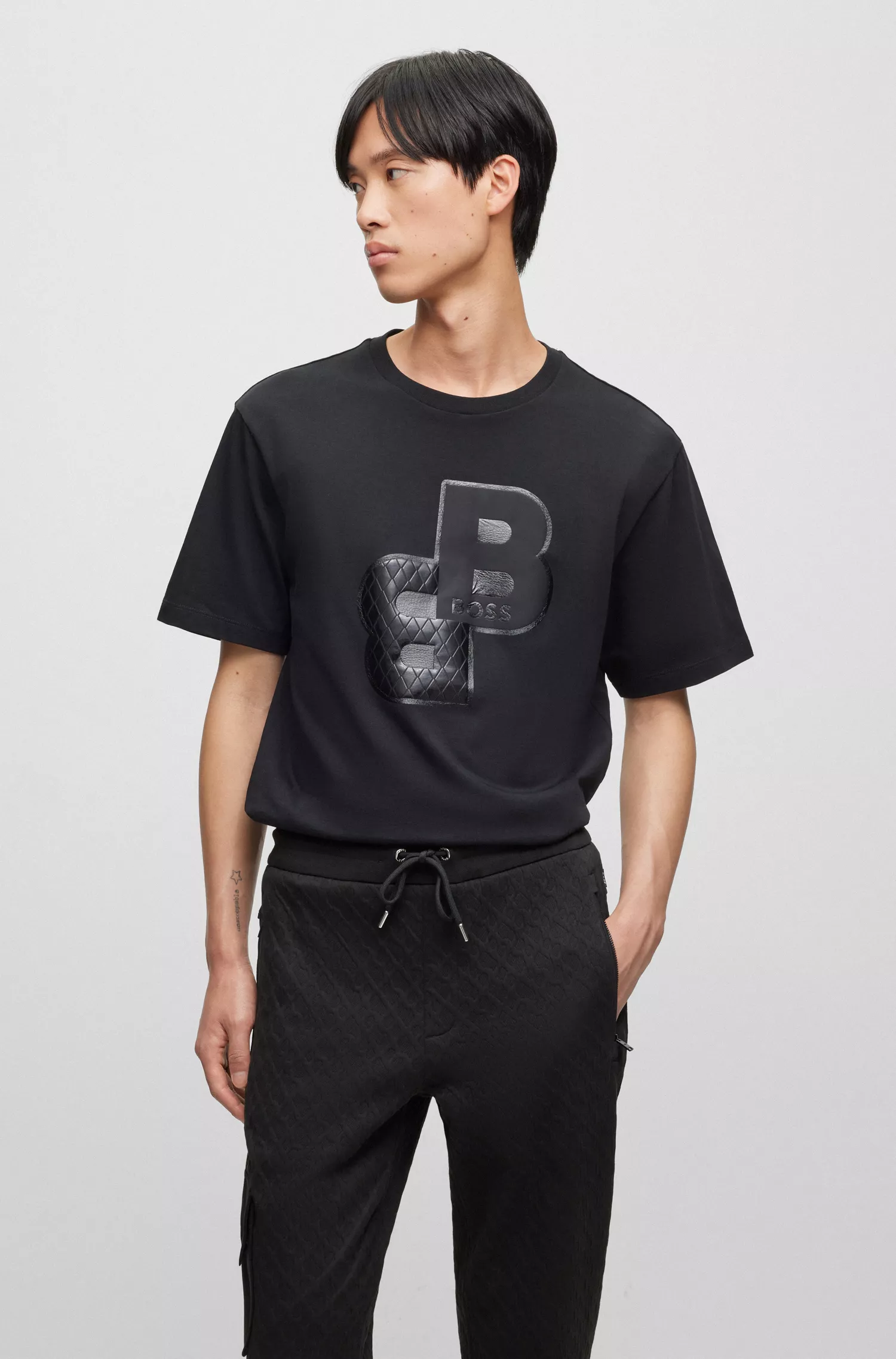 Camiseta BOSS preta em malha de algodão com monogramas estampados em cores variadas.