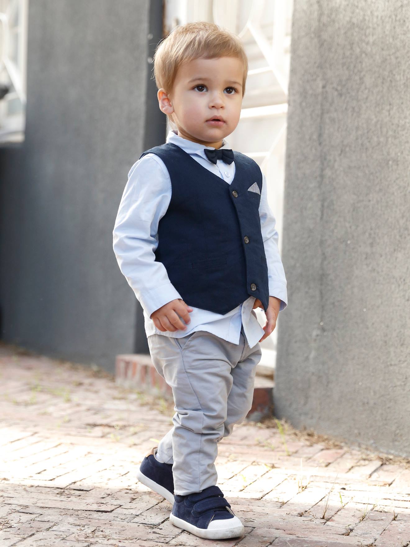 Conjunto formal para bebê menino com colete de tricô, camisa, gravata borboleta e calça azul-escura lisa.