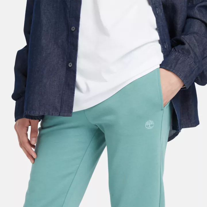 Calça de fato de treino feminina com bordado de árvore na cor verde-azulada.