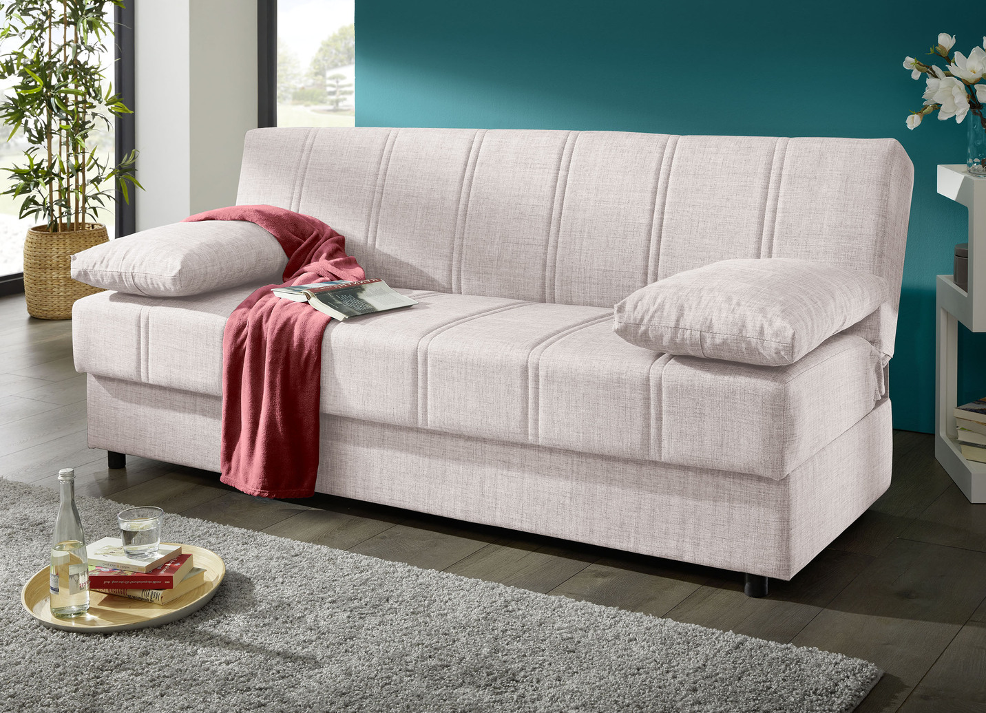 Frei im Raum aufstellbares Schlafsofa mit Dekokissen und Bettkasten