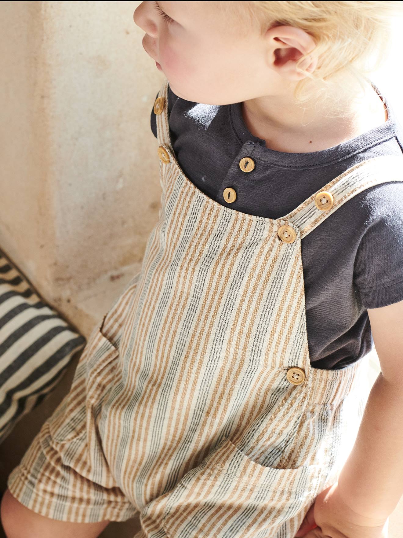 Roupa de bebê: camiseta listrada bege e jardineira.
