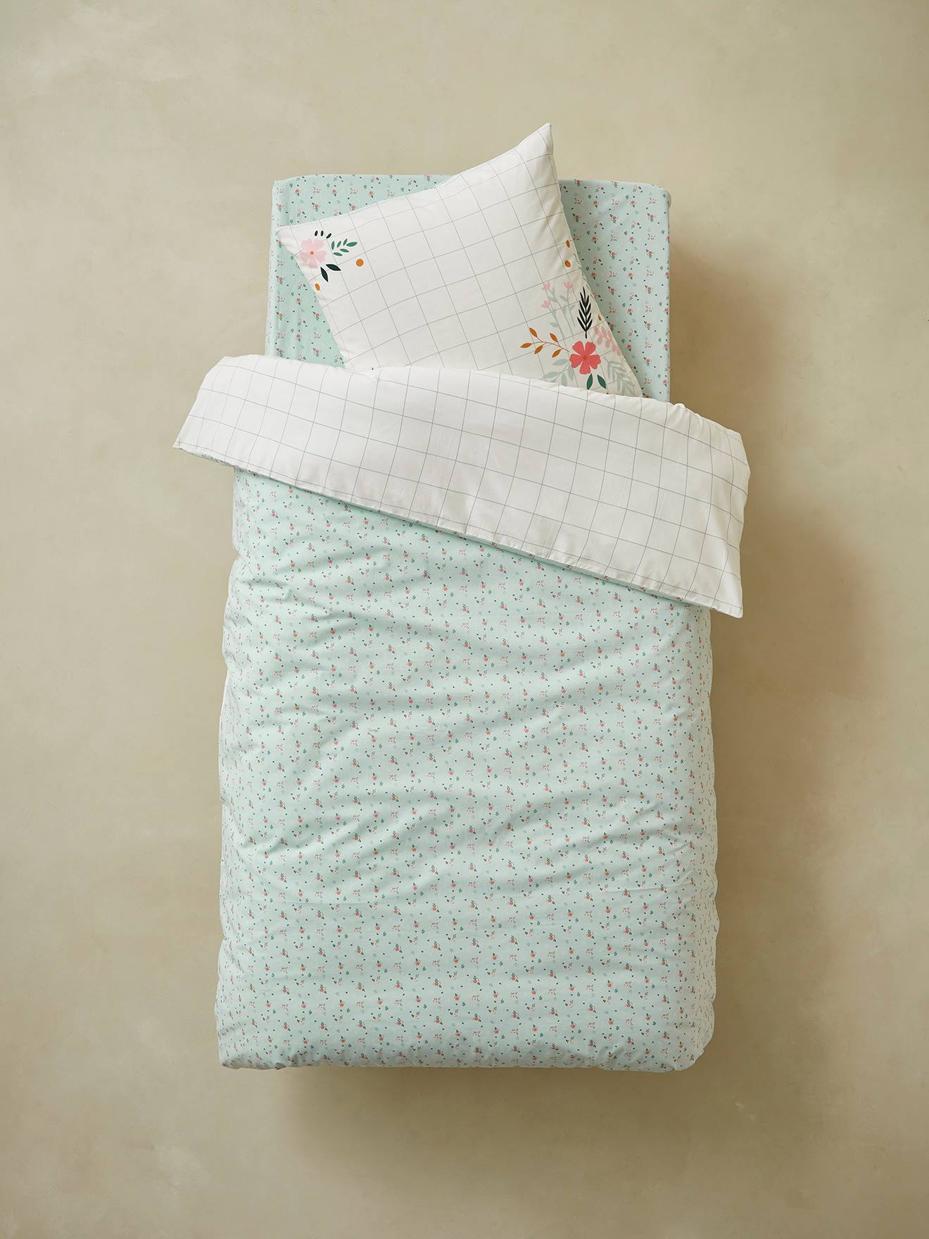 Conjunto de capa de edredom e fronha infantil em algodão orgânico, com estampa floral lisa em branco claro.