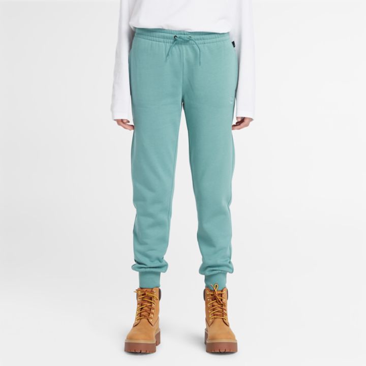 Calça de fato de treino feminina com bordado de árvore na cor verde-azulada.