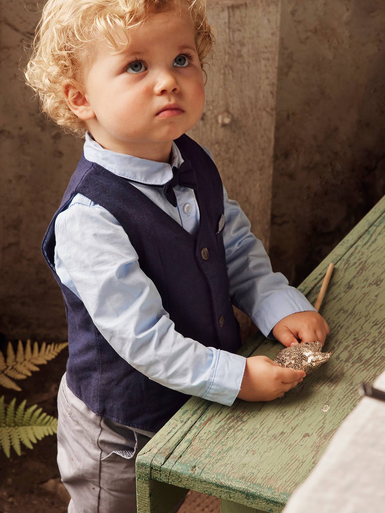 Conjunto formal para bebê menino com colete de tricô, camisa, gravata borboleta e calça azul-escura lisa.