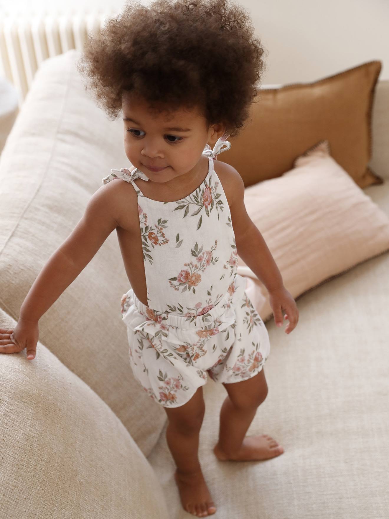 Macacão branco para bebê com estampa floral e suspensórios.