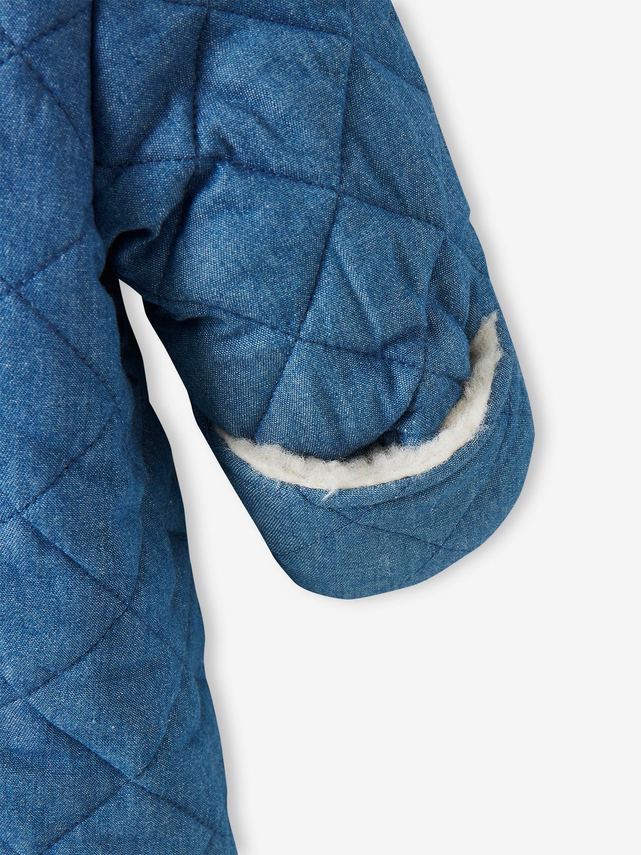 Macacão jeans chambray azul médio para bebê menina, estilo piloto, com abertura assimétrica.