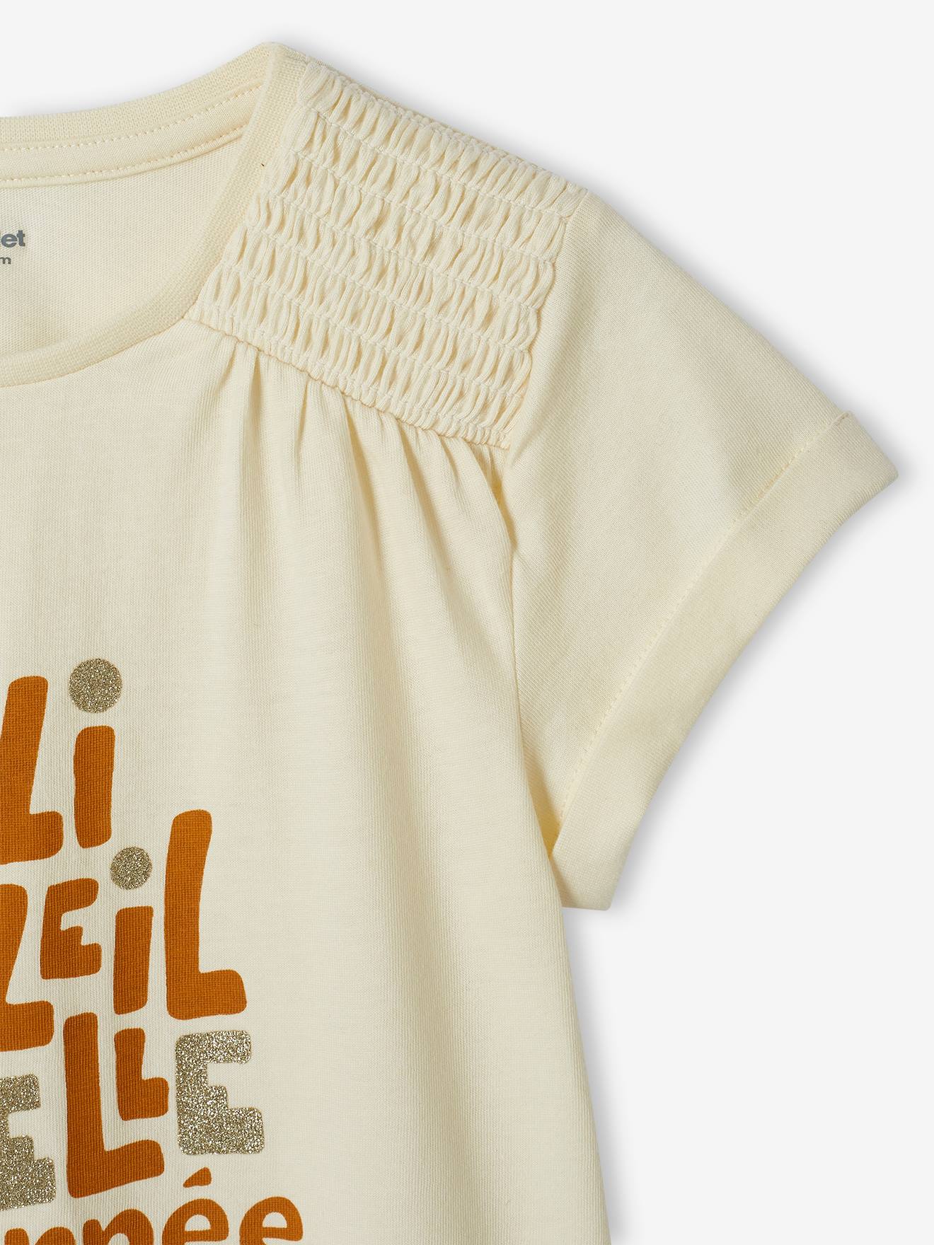 Camiseta infantil bege cru com estampa iridescente e ombros franzidos.