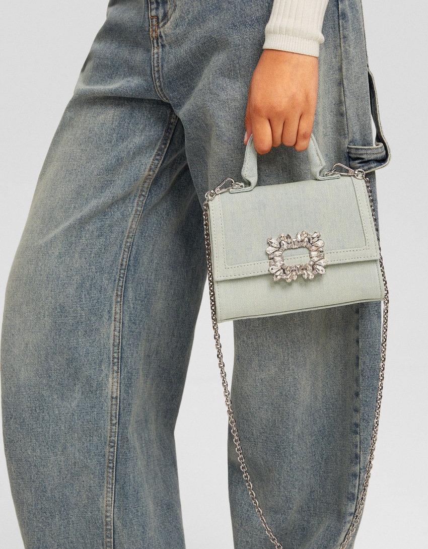 Bolsa transversal multifuncional em jeans com aplicações de miçangas e corrente.