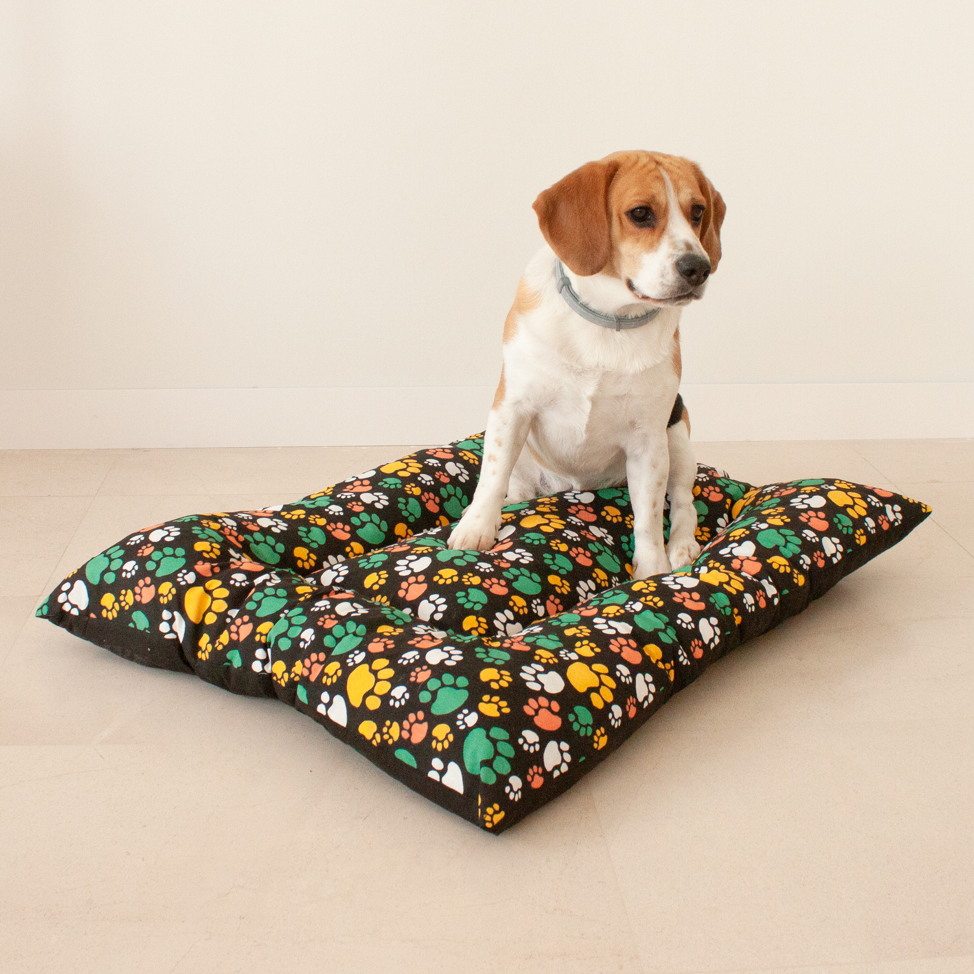 Almofada grande acolchoada para animais de estimação. Preta com estampas de patas multicoloridas. 85x70x10 cm