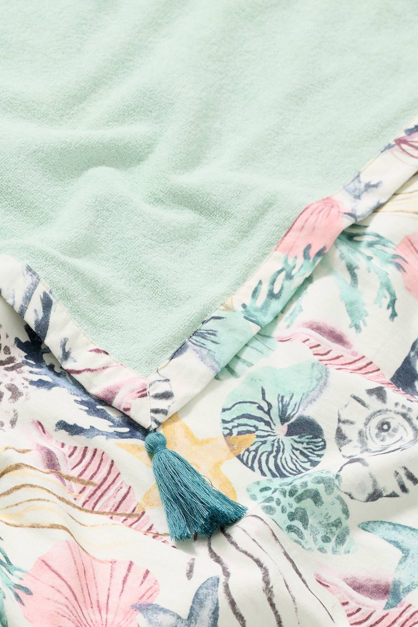 Toalha de praia estampada com conchas e tecido atoalhado.