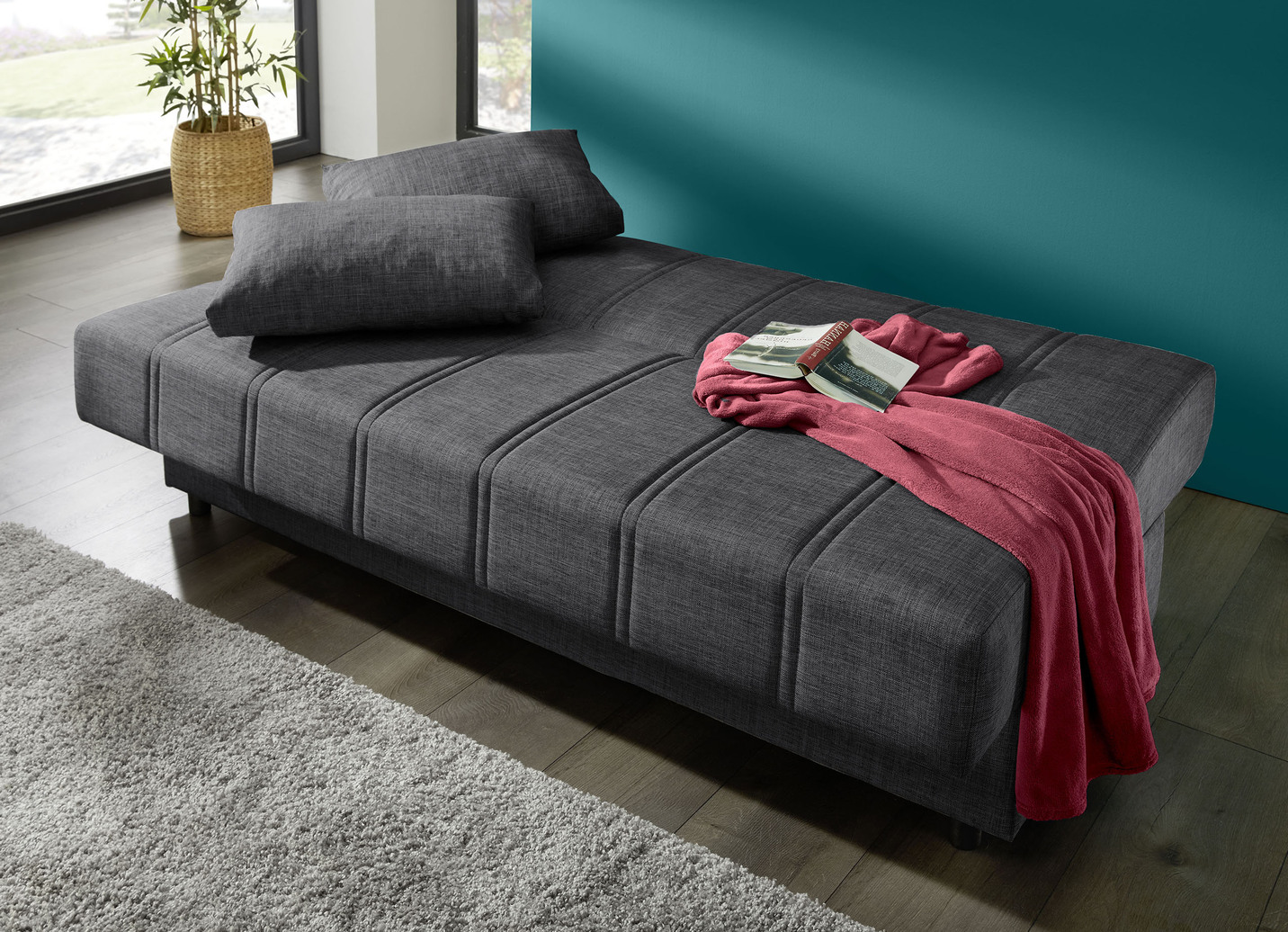 Frei im Raum aufstellbares Schlafsofa mit Dekokissen und Bettkasten