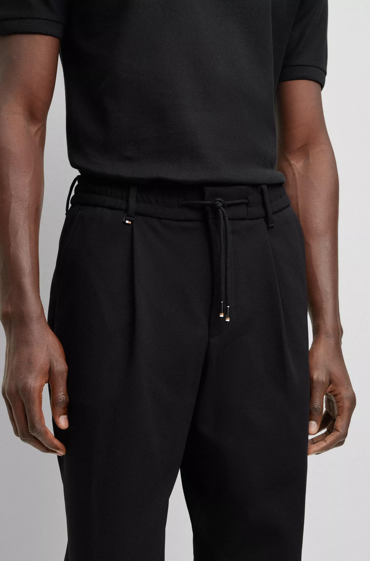 Calça BOSS preta de corte relaxado em tecido elástico com prega frontal.