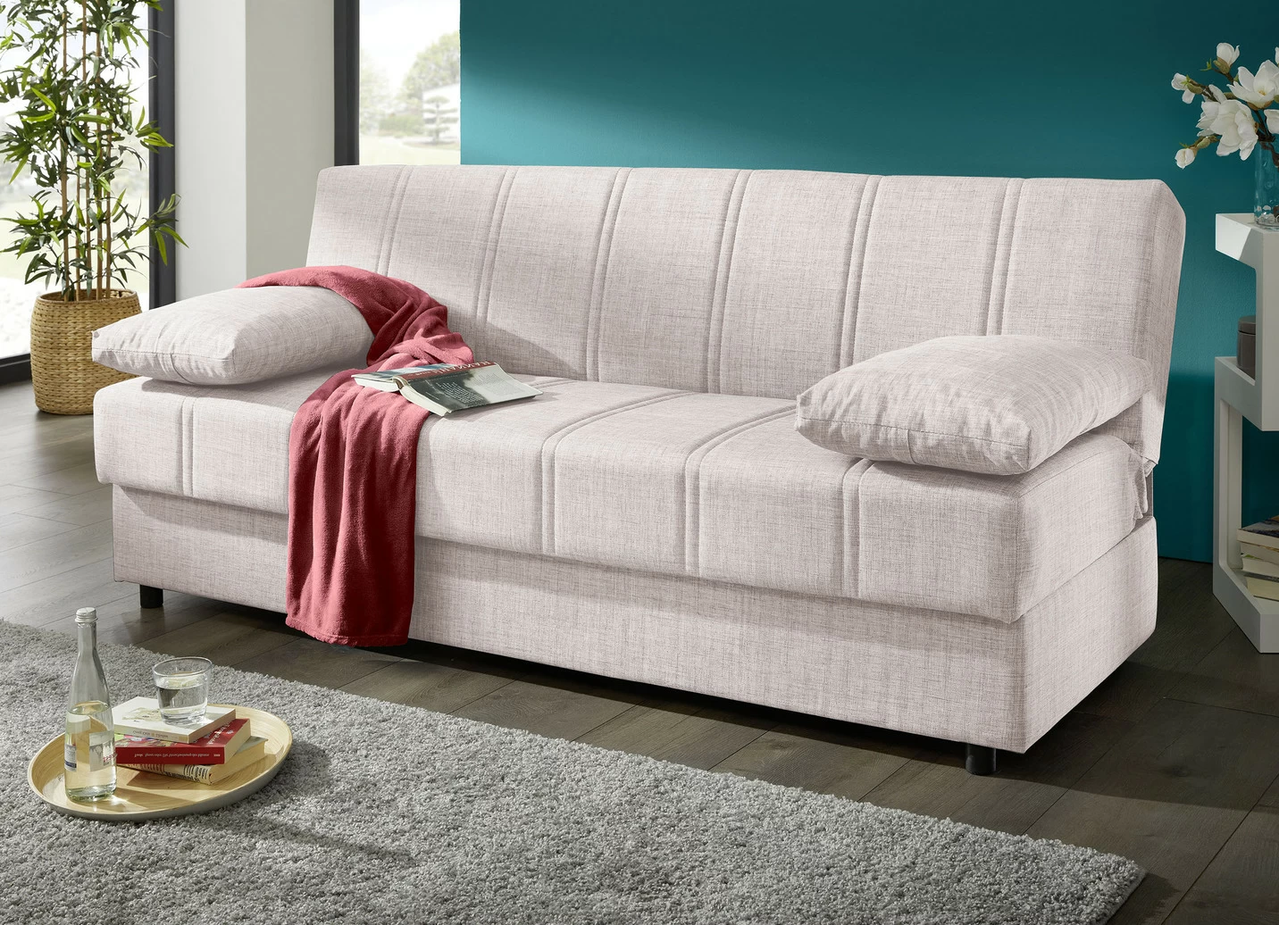 Frei im Raum aufstellbares Schlafsofa mit Dekokissen und Bettkasten