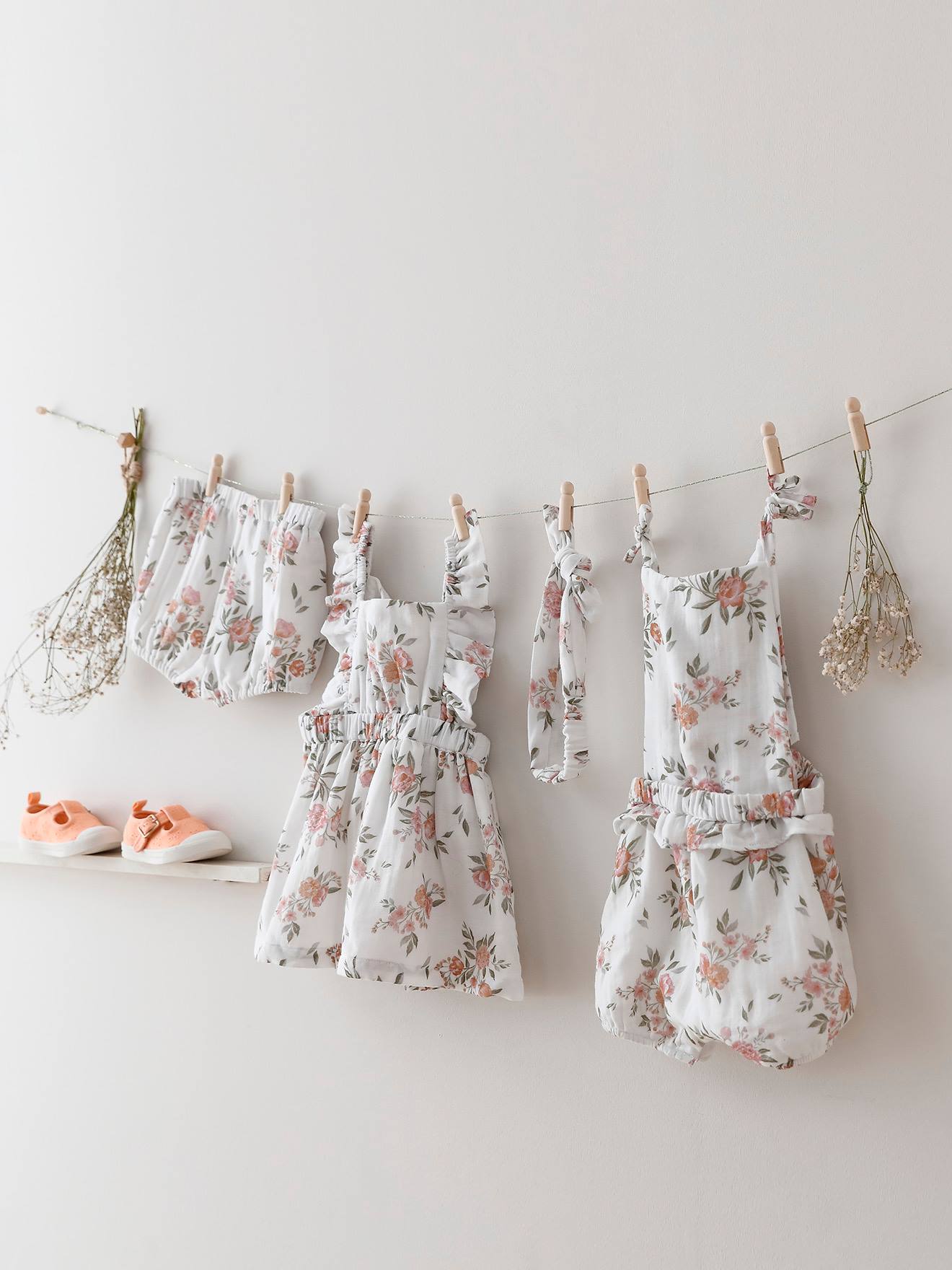 Macacão branco para bebê com estampa floral e suspensórios.