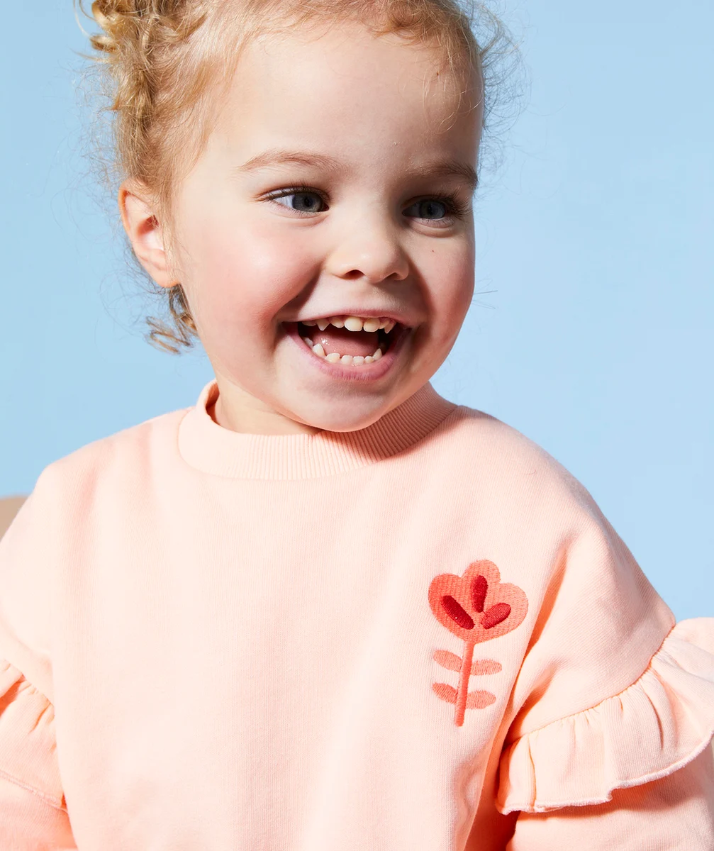 sweat bébé fille en fibres recyclées orange pâle avec volants et fleur brodée