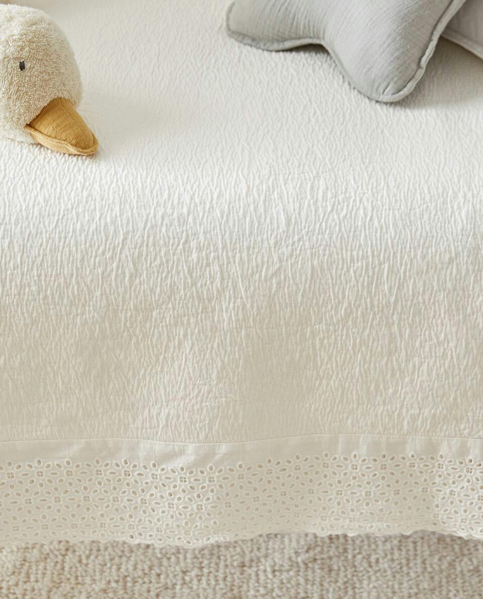 Colcha de algodão com detalhes bordados e franzidos.