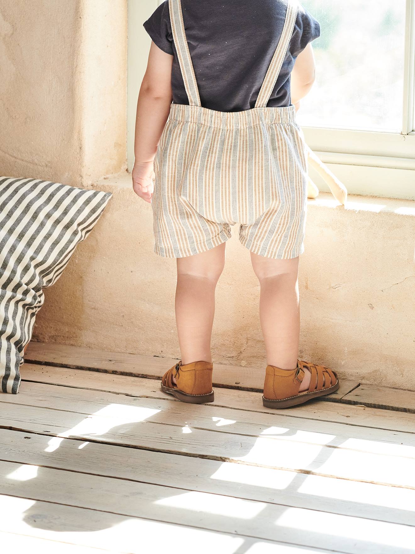 Roupa de bebê: camiseta listrada bege e jardineira.