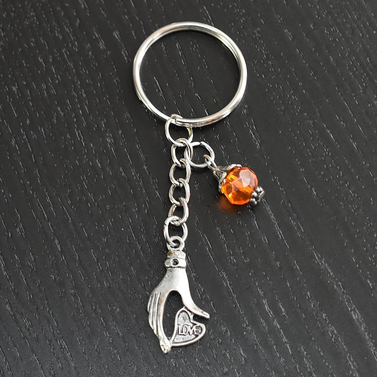 Porte-clés main qui tient un coeur love argentée et perle à facettes orange